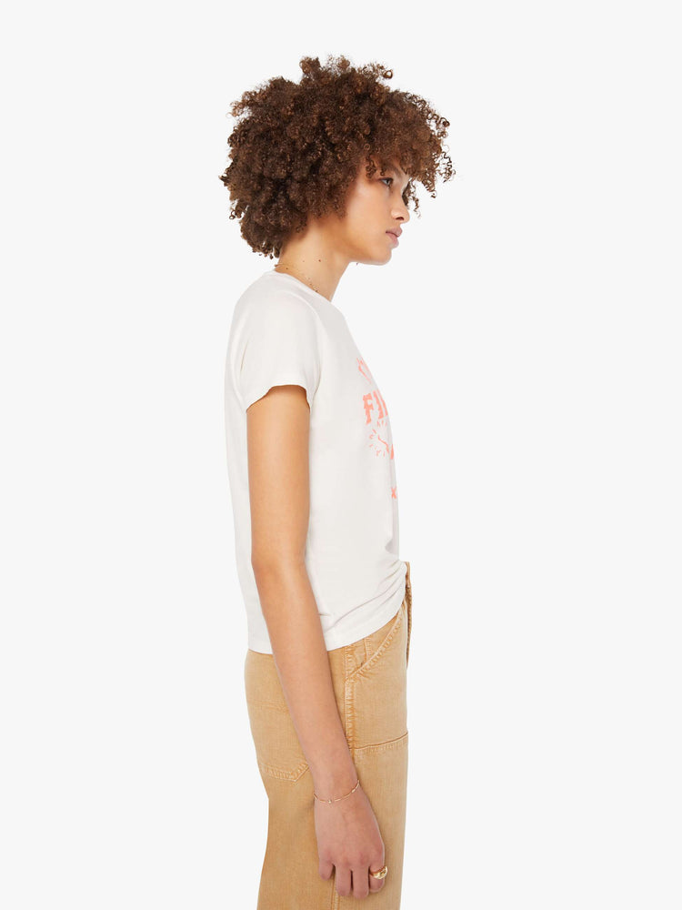 Side view of a woman in white with a faded peach text graphic on the front crewneck tee.