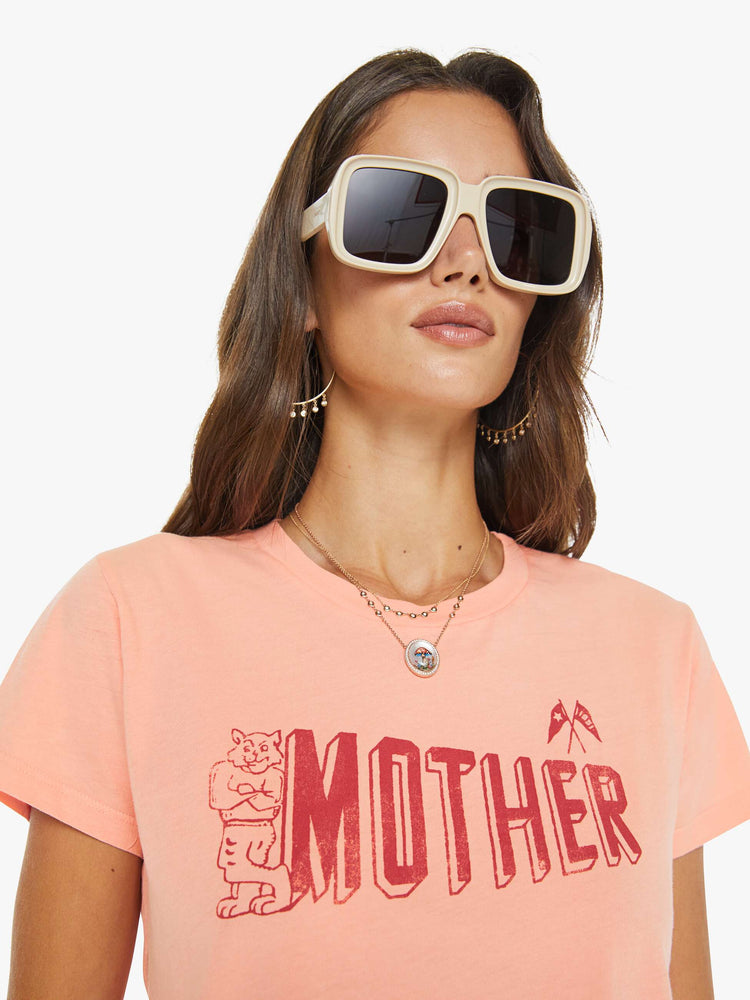 Close up view of a woman in a peach tee features a small cat and MOTHER's name in red on the front.