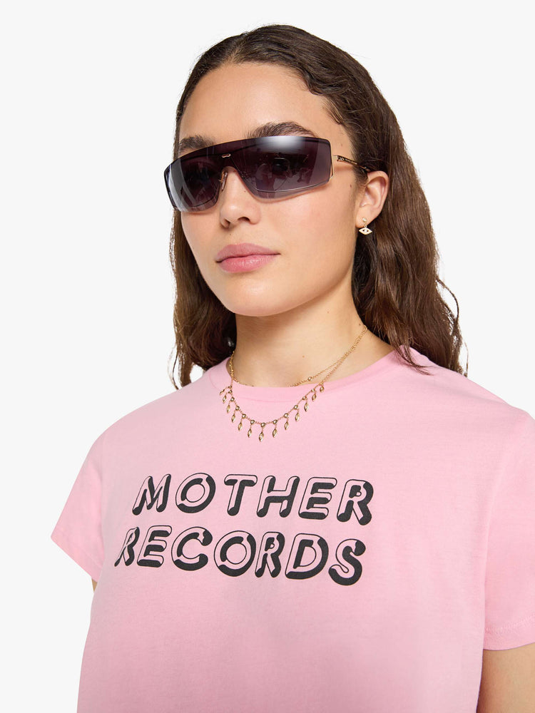 Close up view of a woman in a baby pink tee with a text graphic in black across the front.