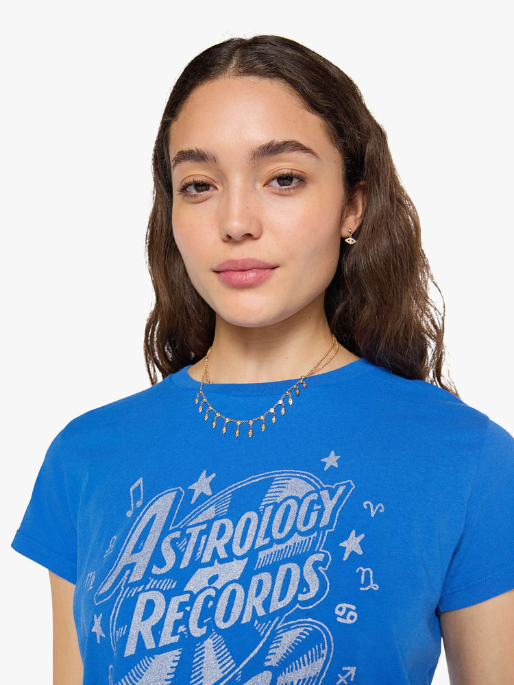 Close up view of a woman in a primary blue tee is designed with a glittery silver graphic inspired by a vintage record store.