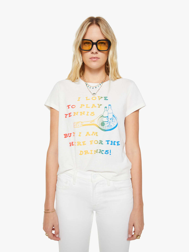 Front view of a woman in a white tee that features  a multi-color text graphic with a tennis racket and cocktails on the front.