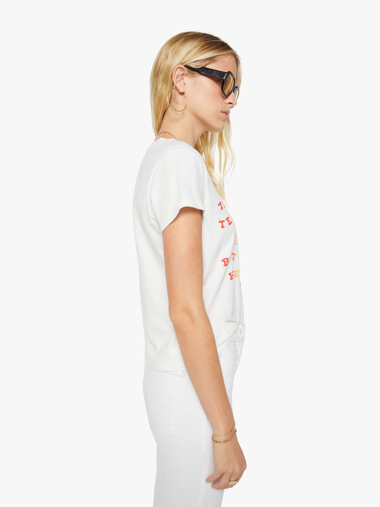 Side view of a woman in a white tee that features  a multi-color text graphic with a tennis racket and cocktails on the front.