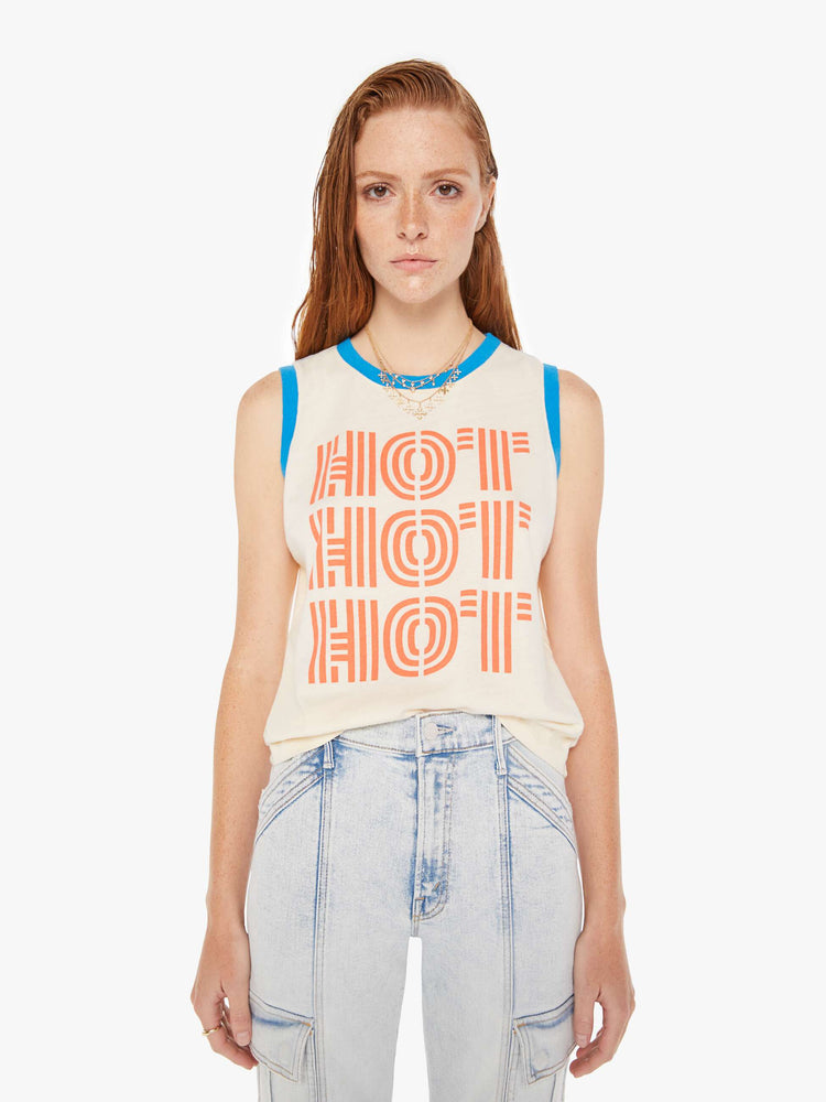 A front view of a woman wearing an off white ringer tank featuring contrast blue trim and a red graphic reading "HOT HOT HOT", paired with a light blue wash jean.