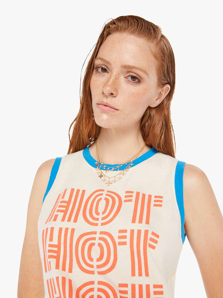 A front close up view of a woman wearing an off white ringer tank featuring contrast blue trim and a red graphic reading "HOT HOT HOT".