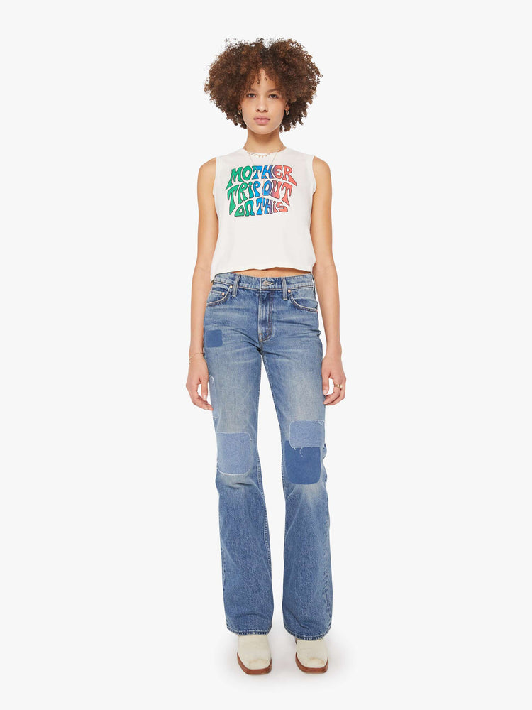 Full body view of a woman in a cropped muscle tee in white with a trippy text graphic on the front.