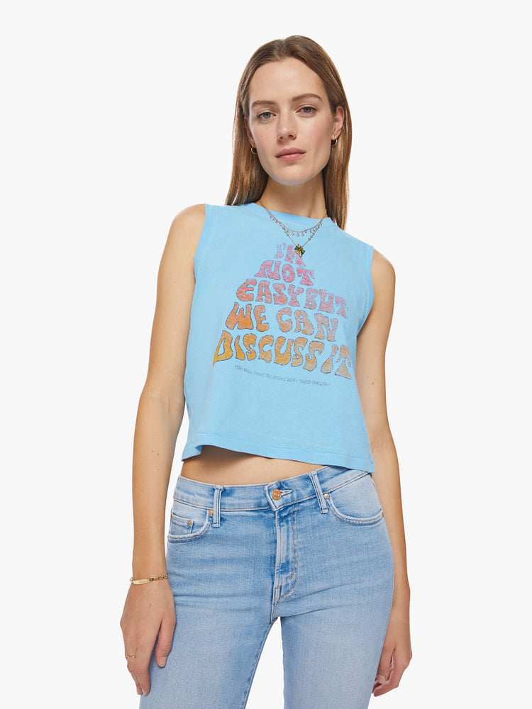 Front view of a woman  cropped muscle tee with a crewneck and boxy fit in baby-blue tank with a text graphic in a warm gradient hues.