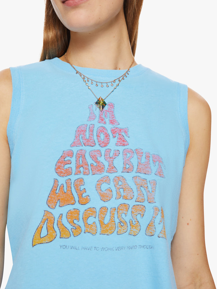 Close up view of a woman cropped muscle tee with a crewneck and boxy fit in baby-blue tank with a text graphic in a warm gradient hues.