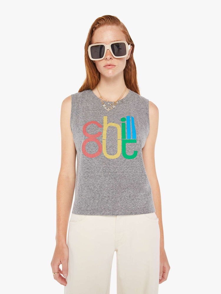 A front view of a woman wearing a heather grey crew neck tank featuring a colorful graphic reading "chill out", paired with off white jeans.