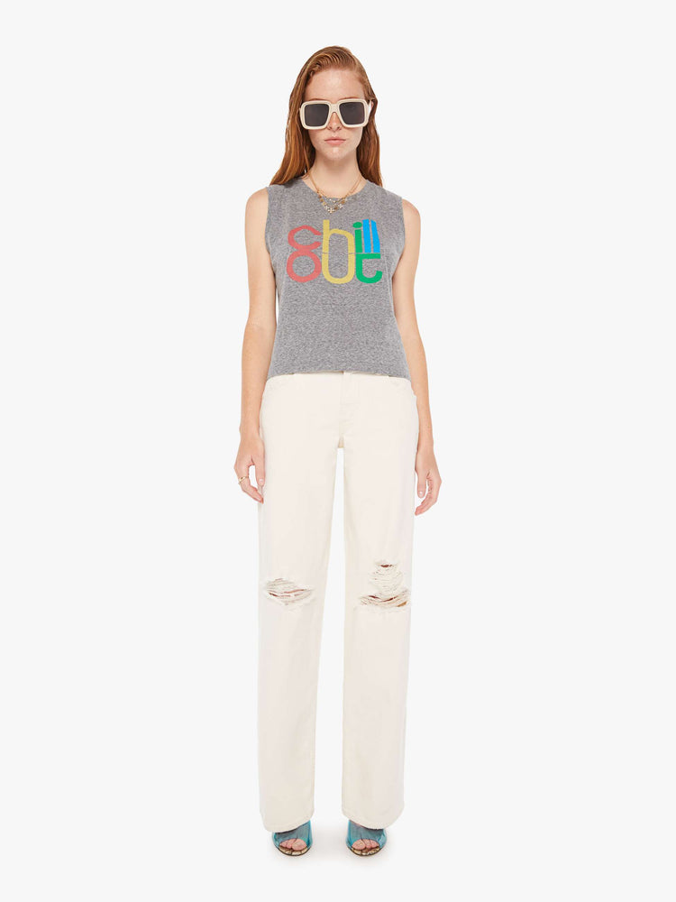 A front full body view of a woman wearing a heather grey crew neck tank featuring a colorful graphic reading "chill out", paired with off white jeans.