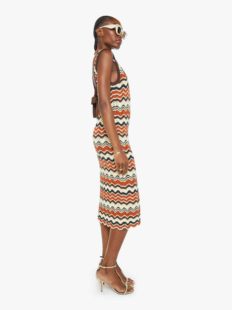 Side view of a woman in a striped graphic print sleeveless midi dress with a scoop neck, narrow fit and scalloped hem that hits at the calf.