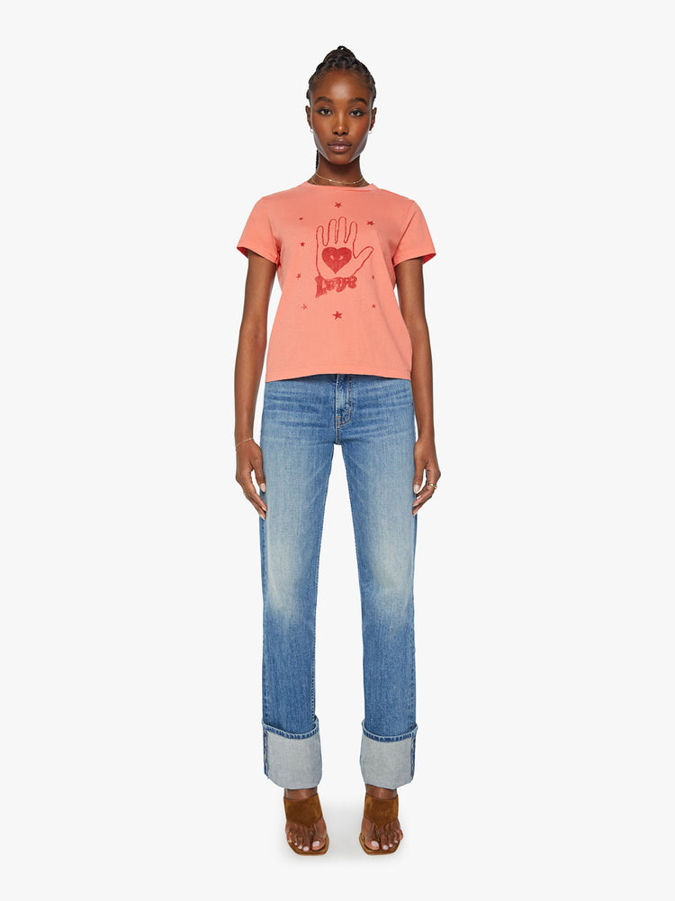 Full body view of a woman orange tee offers a sign of love with a red hand-drawn graphic on the front.