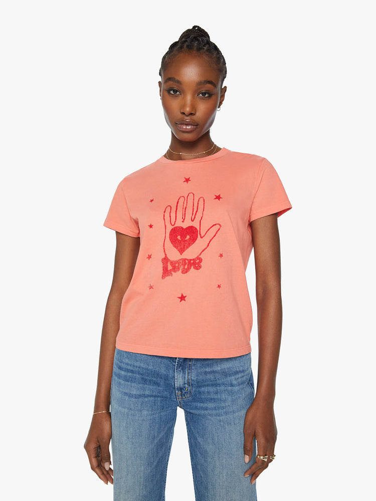Front view of a woman orange tee offers a sign of love with a red hand-drawn graphic on the front.