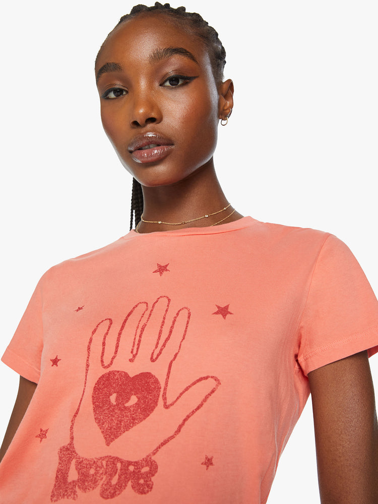 Close up view of a woman orange tee offers a sign of love with a red hand-drawn graphic on the front.