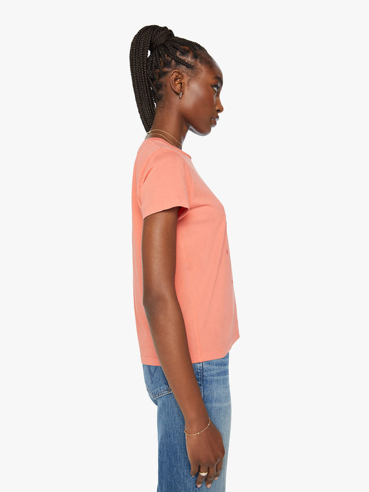 Side view of a woman orange tee offers a sign of love with a red hand-drawn graphic on the front.