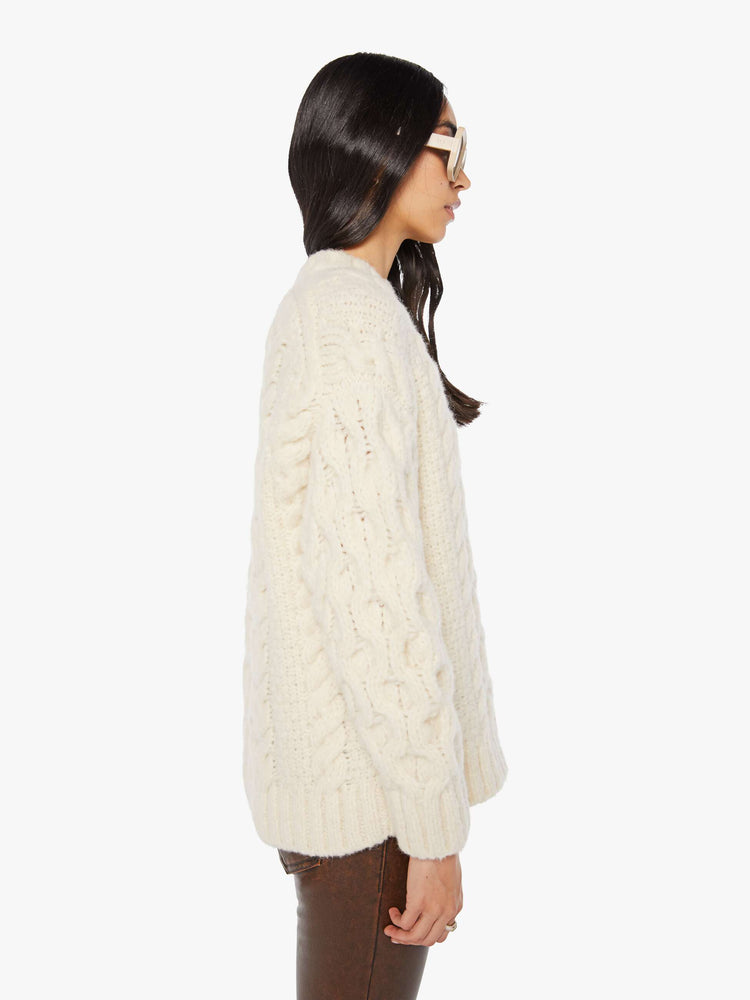Side view of a woman in an off white cable crewneck sweater in MOTHERS  stitched in black.
