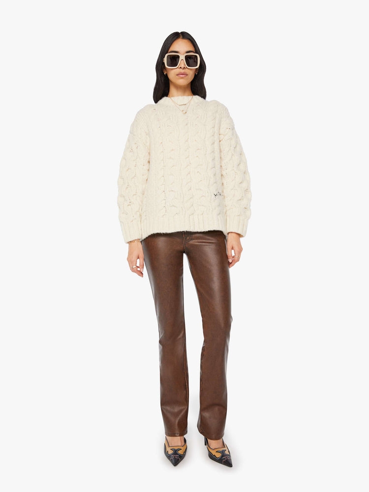 Full body view of a woman in an off white cable crewneck sweater in MOTHERS  stitched in black.