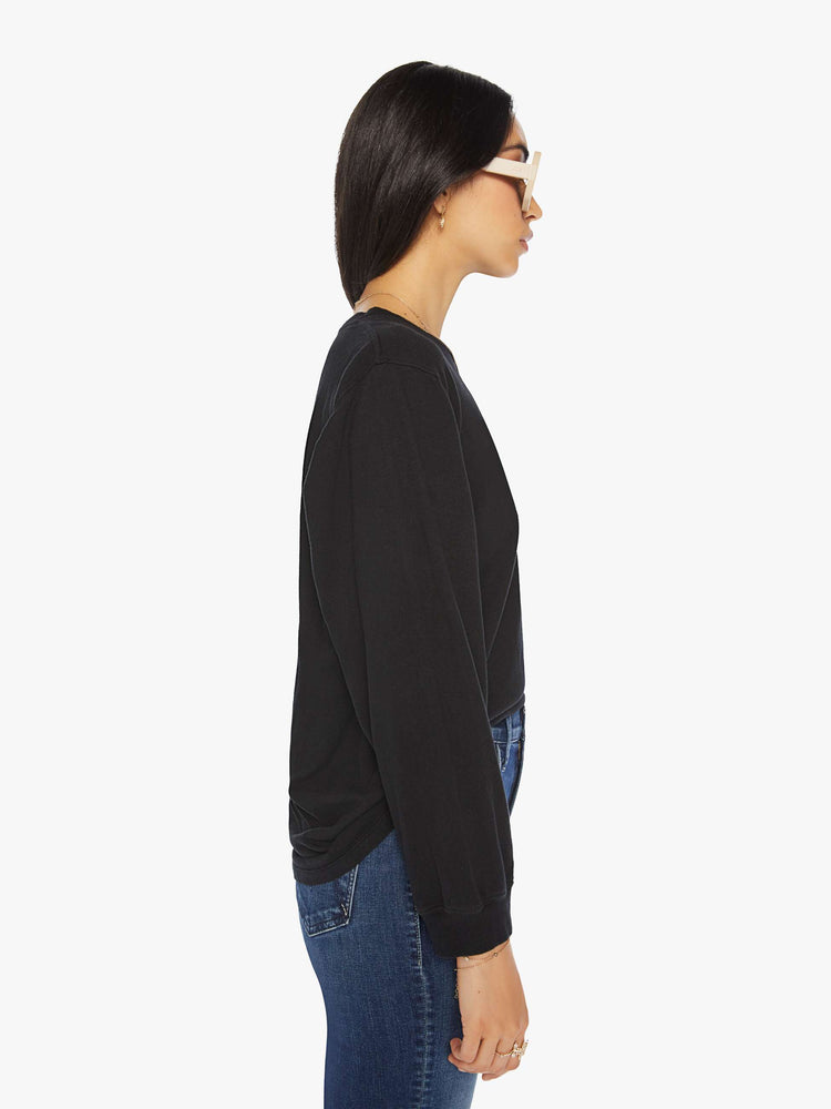 Side view of a woman black crewneck tee with long sleeves and an oversized fit.