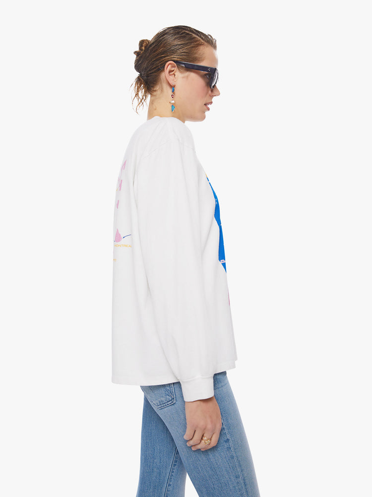 Side view of a woman oversized long sleeve tee in white, the tee features a colorful graphic that channels the electrifying spirit of the tour.