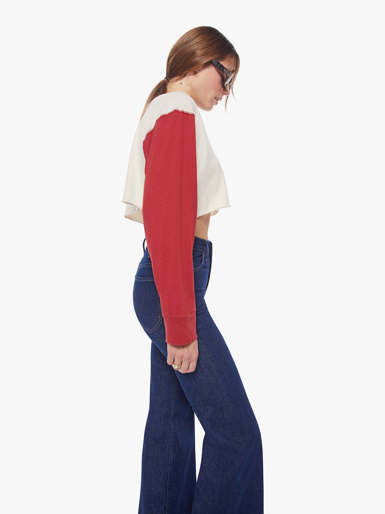Side view of a woman longsleeve tee with a scoop neck, long sleeves, drop shoulders and a super-cropped hem in an off-white hue with red sleeves.