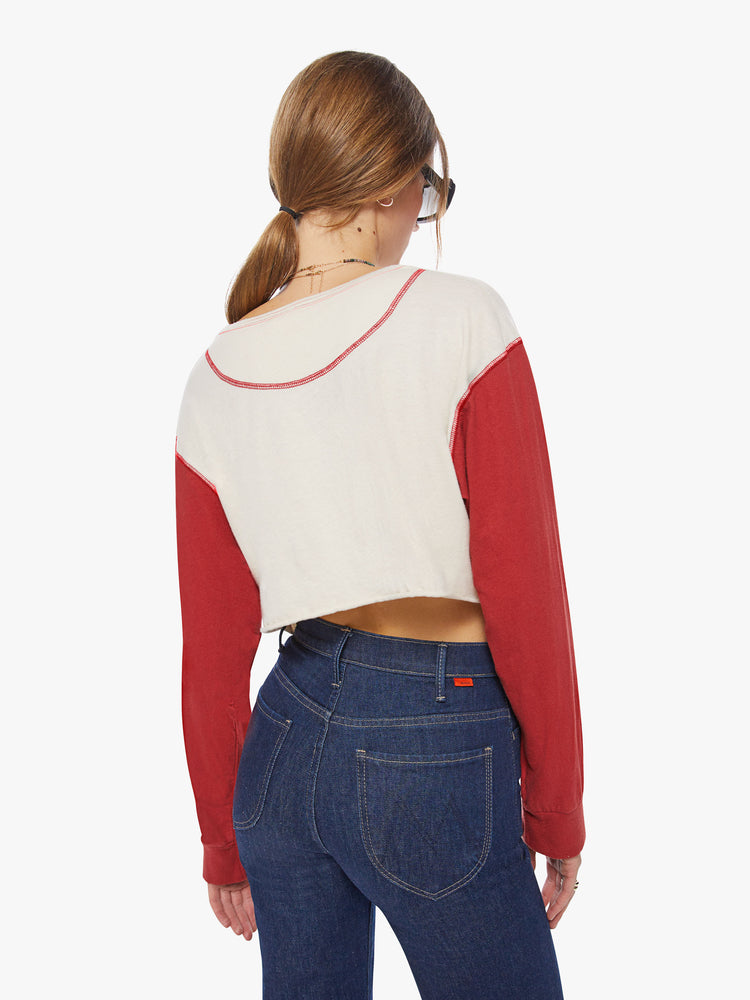 Back view of a woman longsleeve tee with a scoop neck, long sleeves, drop shoulders and a super-cropped hem in an off-white hue with red sleeves.