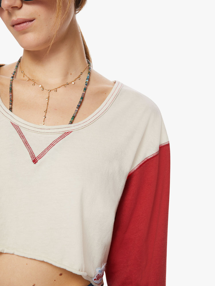 Close up view of a woman longsleeve tee with a scoop neck, long sleeves, drop shoulders and a super-cropped hem in an off-white hue with red sleeves.