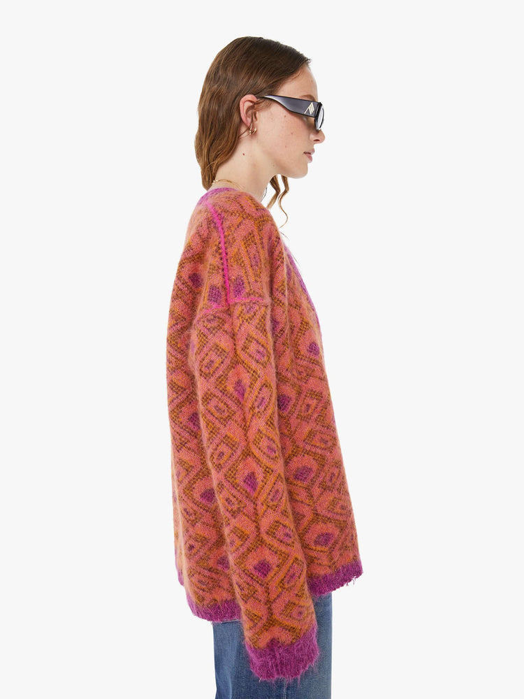 Side view of a woman in a two equally bold sides in an orange, salmon and purple reversible oversized cardigan features a V-neck, drop shoulders, ribbed hems and buttons down the front.