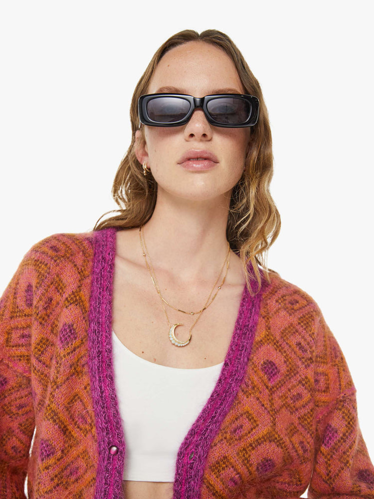 Close up view of a woman in a two equally bold sides in an orange, salmon and purple reversible oversized cardigan features a V-neck, drop shoulders, ribbed hems and buttons down the front.