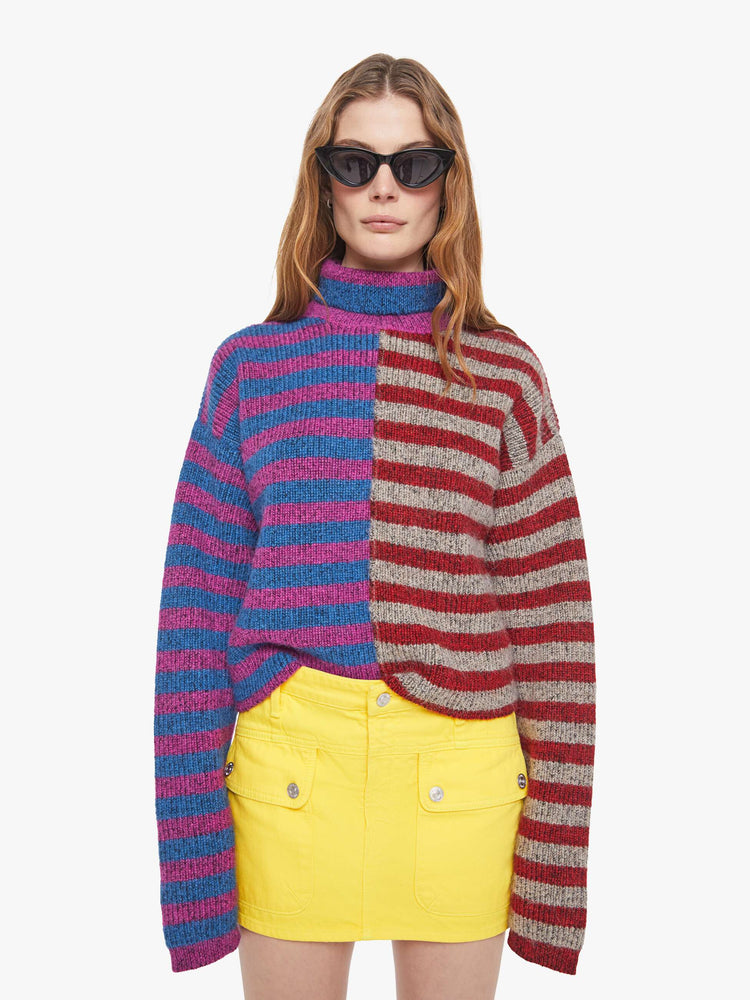 Front view of a woman in a half blue with purple stripes and half grey with red stripes turtleneck sweater with drop shoulders, extra-long sleeves and a boxy fit.