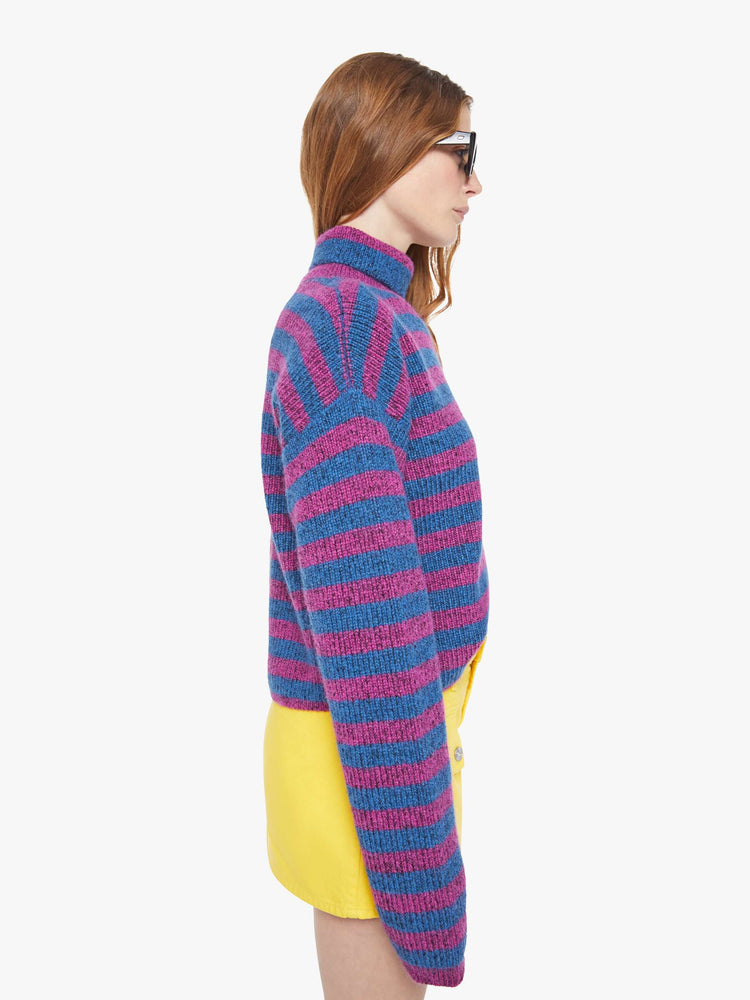 Side view of a woman in a half blue with purple stripes and half grey with red stripes turtleneck sweater with drop shoulders, extra-long sleeves and a boxy fit.