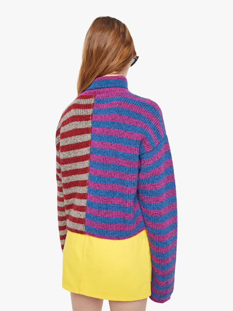 Back view of a woman in a half blue with purple stripes and half grey with red stripes turtleneck sweater with drop shoulders, extra-long sleeves and a boxy fit.