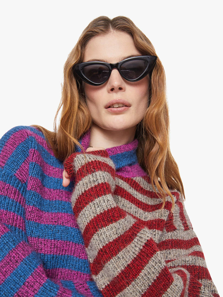 Close up view of a woman in a half blue with purple stripes and half grey with red stripes turtleneck sweater with drop shoulders, extra-long sleeves and a boxy fit.