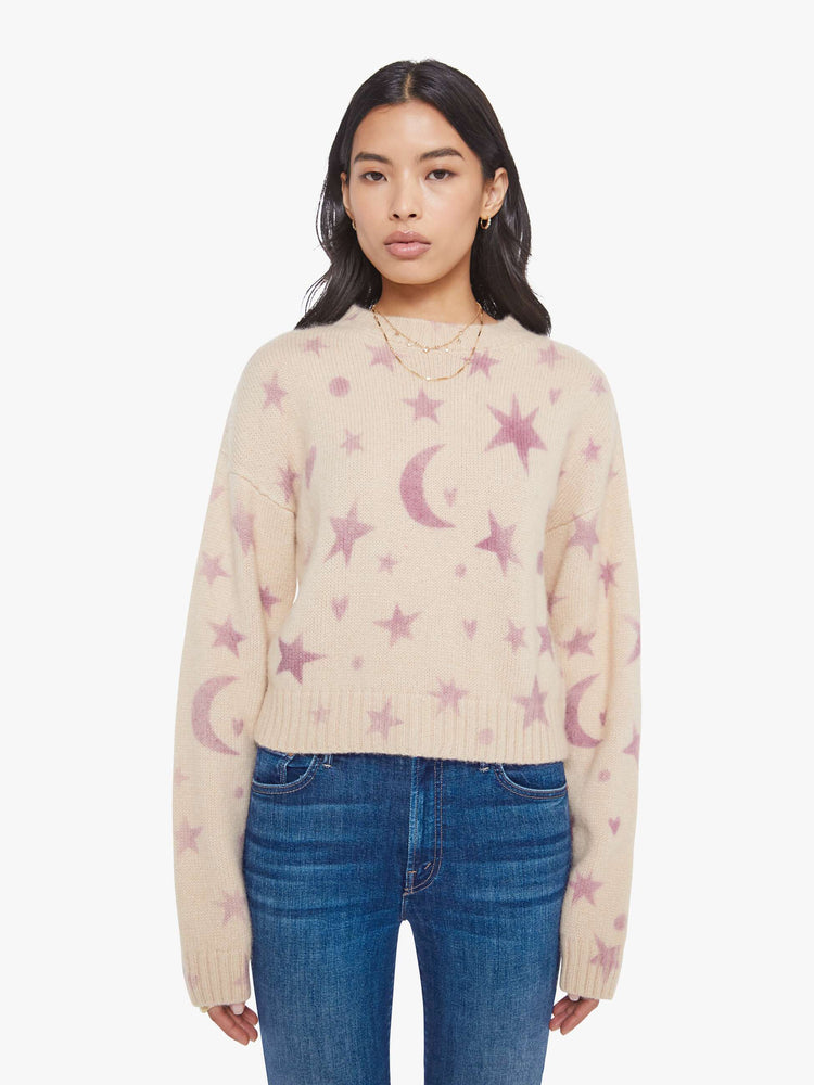 Front view of a woman in a cream with a light pink celestial print throughout crewneck sweater. 