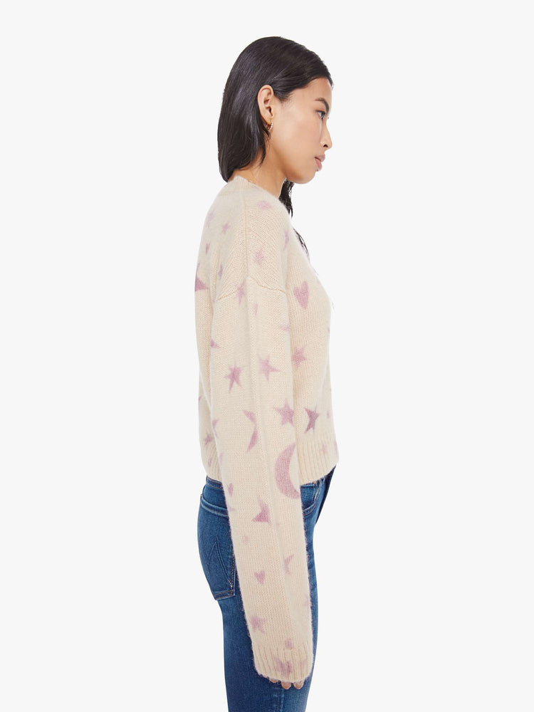 Side view of a woman in a cream with a light pink celestial print throughout crewneck sweater. 