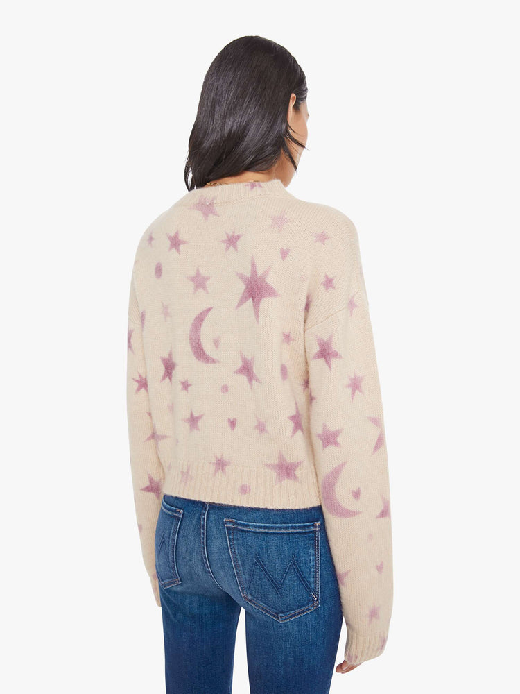 Back view of a woman in a cream with a light pink celestial print throughout crewneck sweater. 