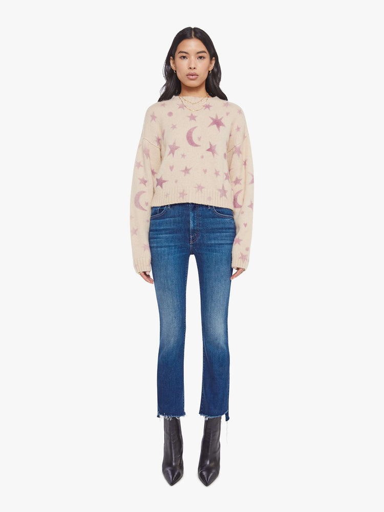 Full body view of a woman in a cream with a light pink celestial print throughout crewneck sweater. 