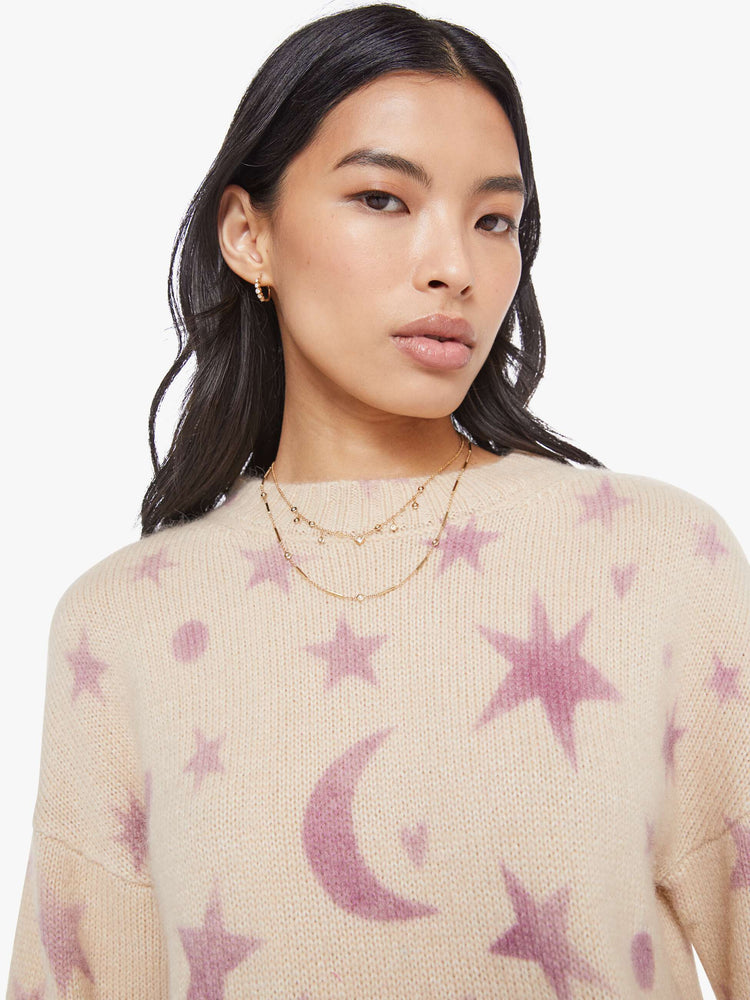 Close up view of a woman in a cream with a light pink celestial print throughout crewneck sweater. 