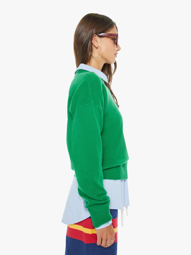 Side view of a woman in a green crewneck sweater with drop shoulders, ribbed hems and an oversized fit.