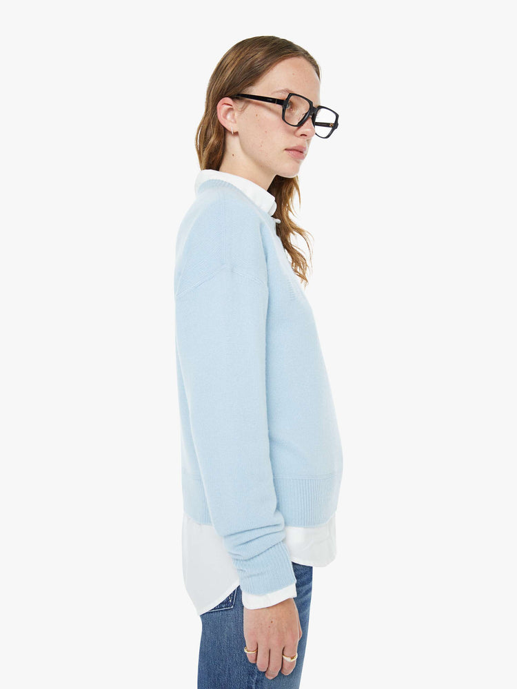 Side view of a woman in a light blue crewneck sweater with drop shoulders, ribbed hems and an oversized fit.