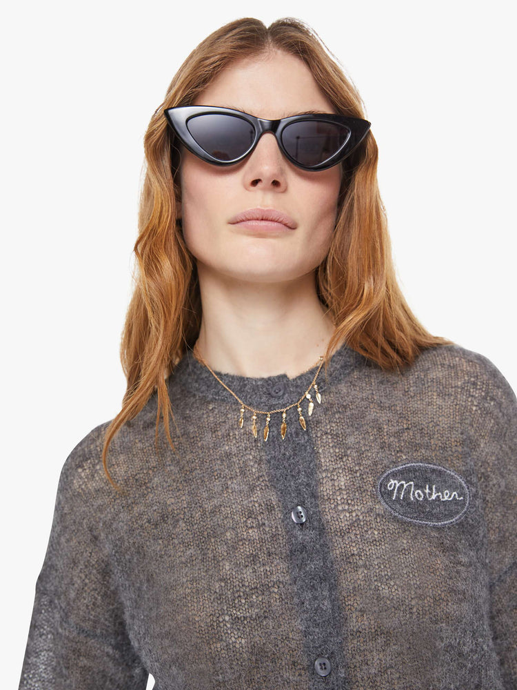 Close up view of a woman in a sheer grey woo cardigan with MOTHERS name patched on the chest.
