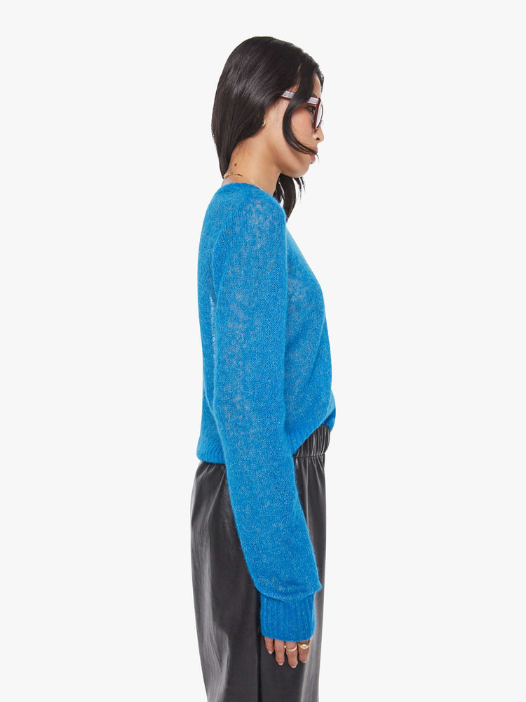 Side view of a woman in a sheer blue with an oval patch on the chest sweater.