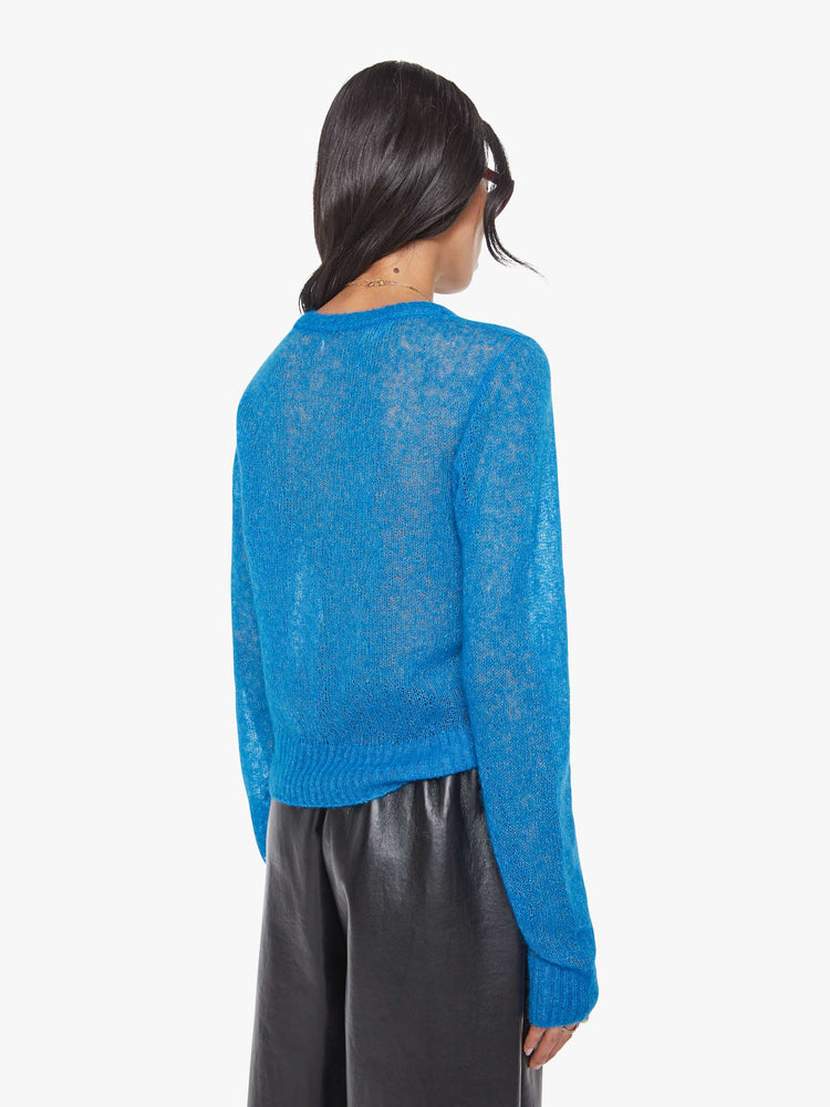 Back view of a woman in a sheer blue with an oval patch on the chest sweater.
