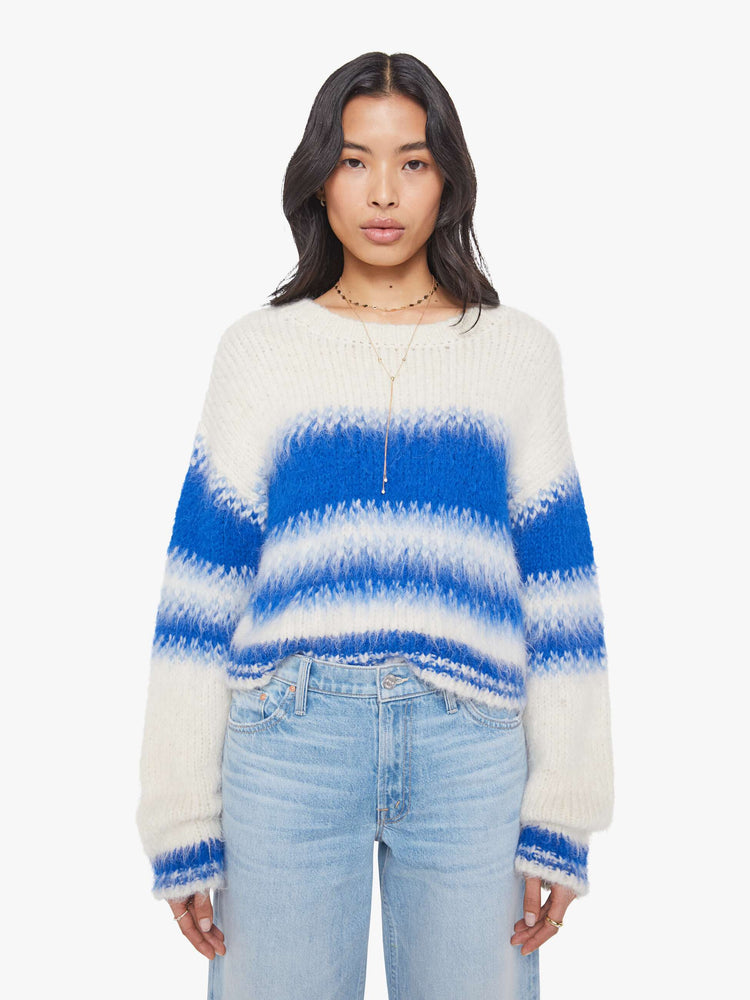Front view of a woman in an off-white with blue stripes crewneck sweater with drop shoulders, thick ribbed hems and a slightly cropped fit. 