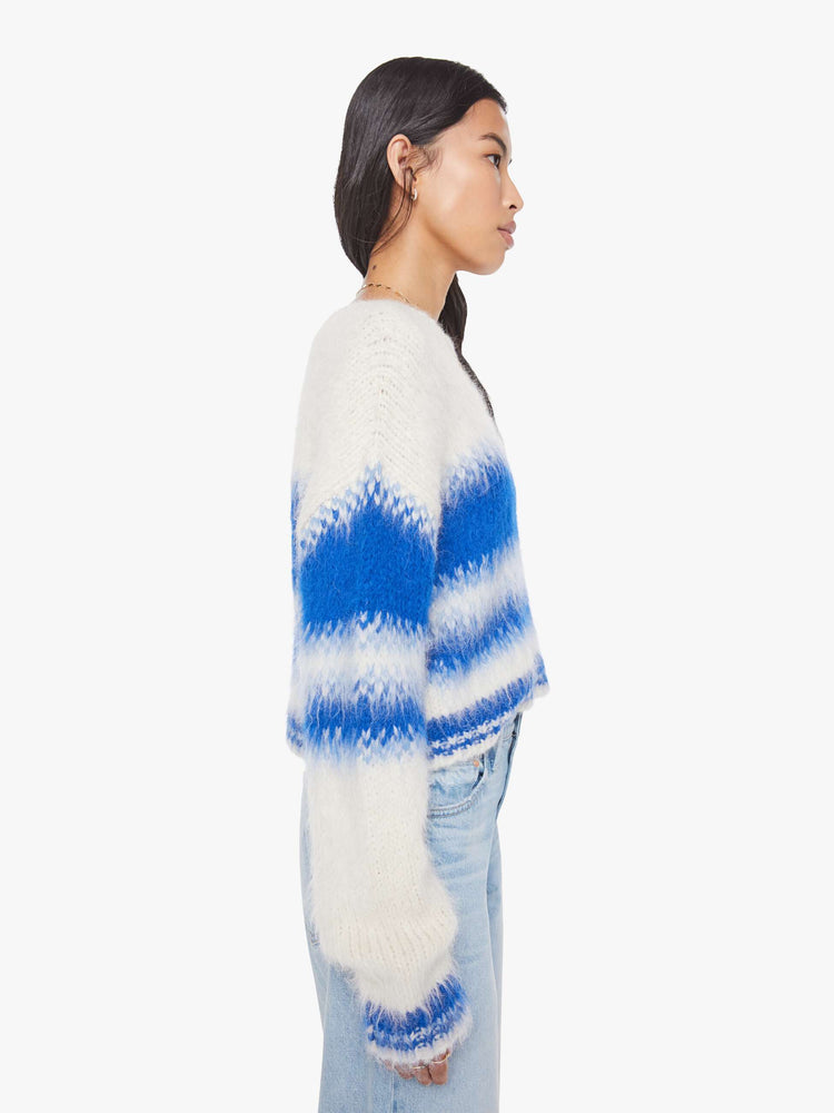 Side view of a woman in an off-white with blue stripes crewneck sweater with drop shoulders, thick ribbed hems and a slightly cropped fit. 