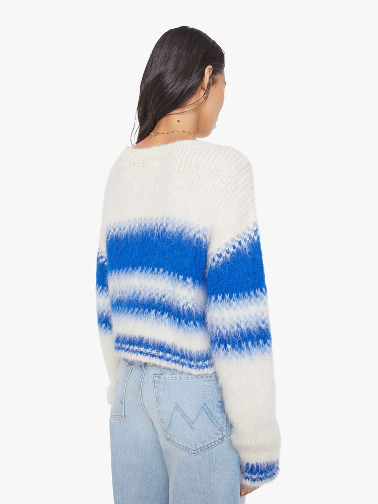 Back view of a woman in an off-white with blue stripes crewneck sweater with drop shoulders, thick ribbed hems and a slightly cropped fit. 