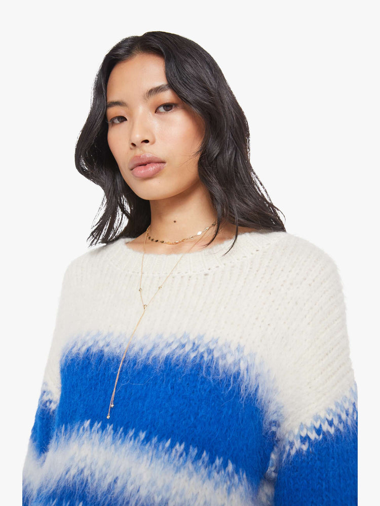 Close up view of a woman in an off-white with blue stripes crewneck sweater with drop shoulders, thick ribbed hems and a slightly cropped fit. 