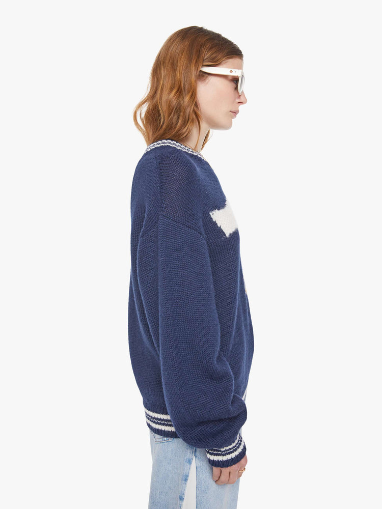 Side view of a woman in a navy sweater with white stripes at the hems and two birds smoking on the front.