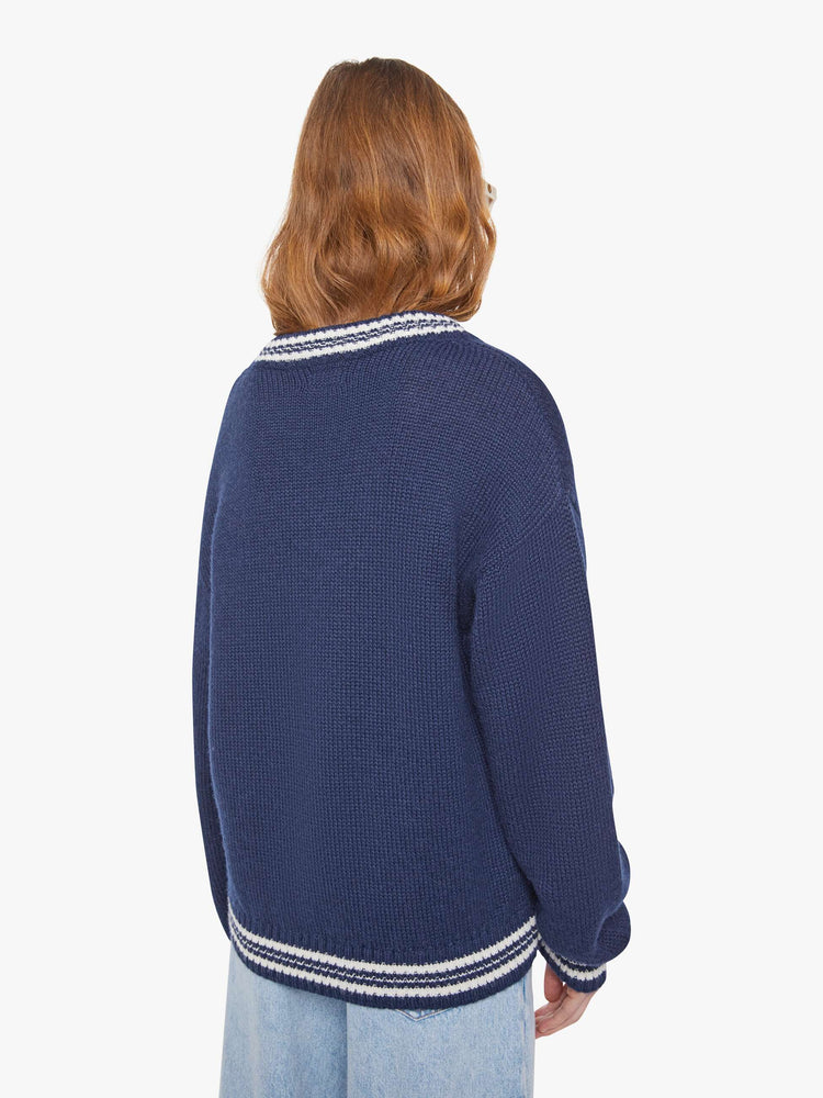 Back view of a woman in a navy sweater with white stripes at the hems and two birds smoking on the front.