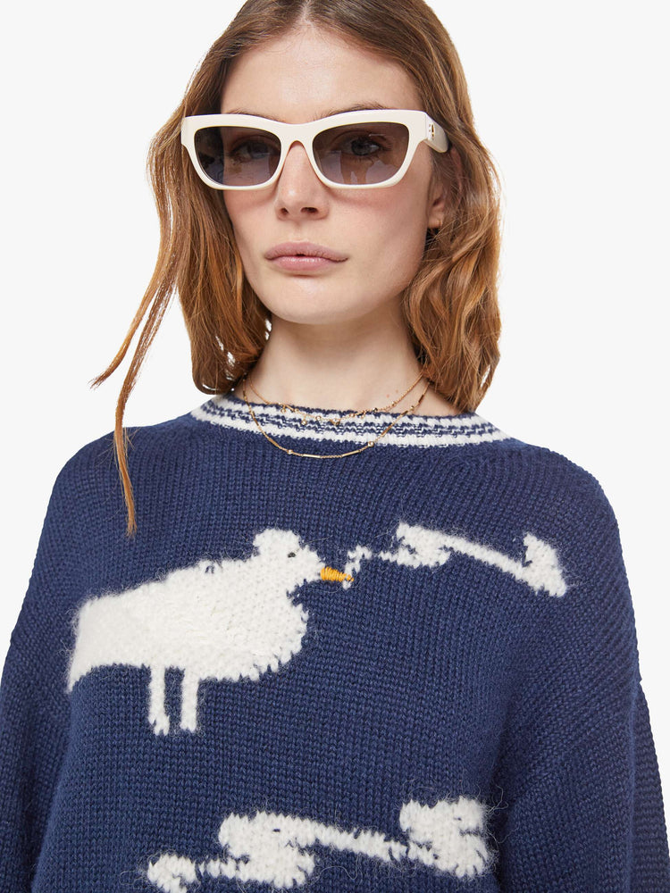 Close up view of a woman in a navy sweater with white stripes at the hems and two birds smoking on the front.