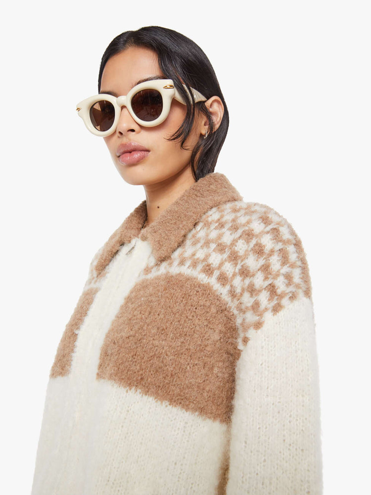 Close up view of a woman in an off white with light khaki details and text on the back collared zip-up cardigan with drop shoulders, ribbed hems and a boxy fit. 