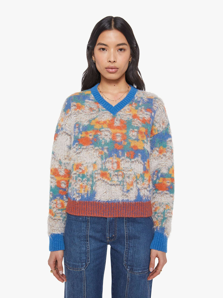 Front view of a woman in a blue, yellow, orange and green graphic print sweater  with fuzzy, distressed details inspired by a well-worn rug. 